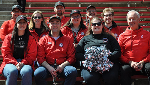 Members of UCBAA band sitting in bleachers, wearing red and black.